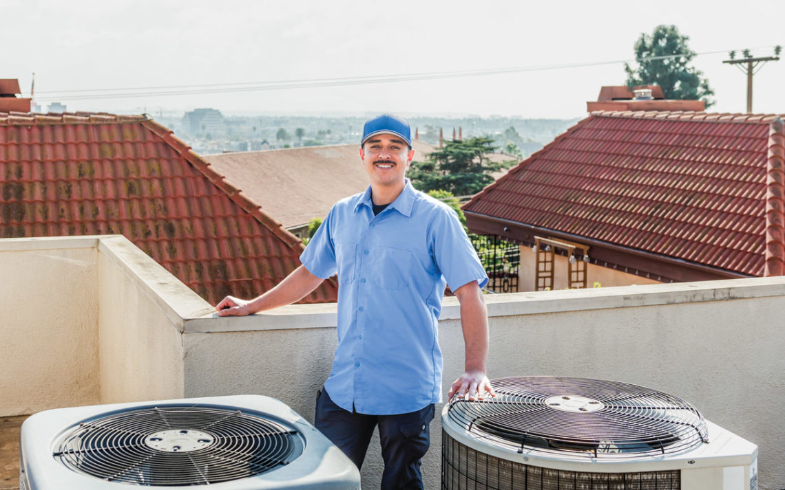 John Castillo, business owner, stands on a roof with his hands resting on two AC units.