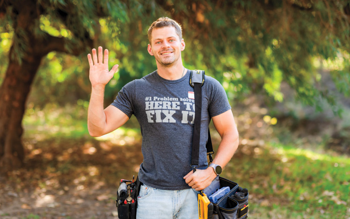 Efim Kostylev stands in a park with a bag belt and tools, waving.