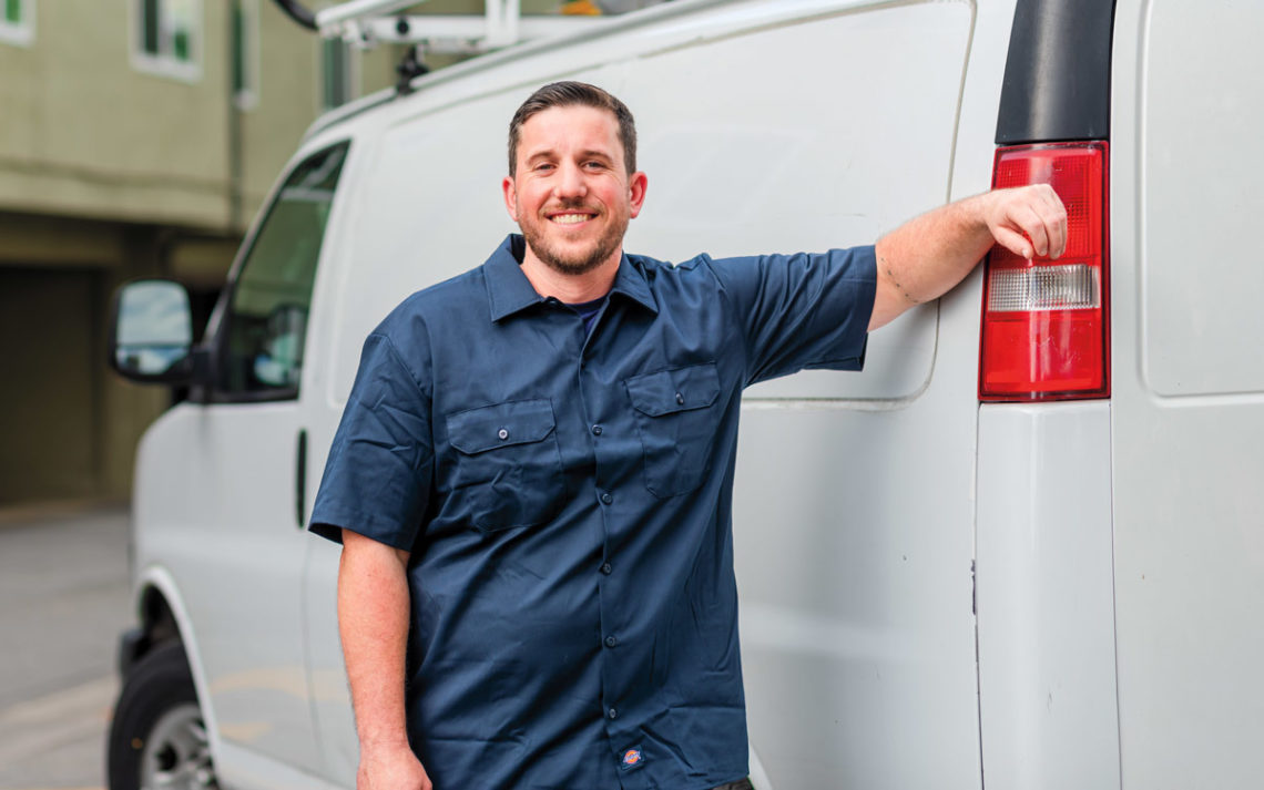 Patrick Hanifan leaning against his van smiling.