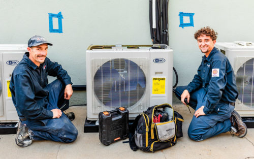Owners kneel beside an HVAC unit with tools around them.