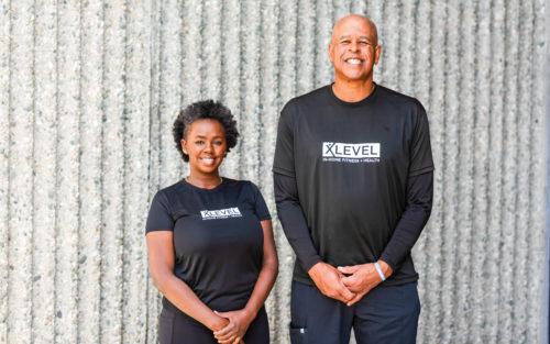 David Cantrell, owner of X Level Fitness, and Sheila Maingi standing together in front of a wall.